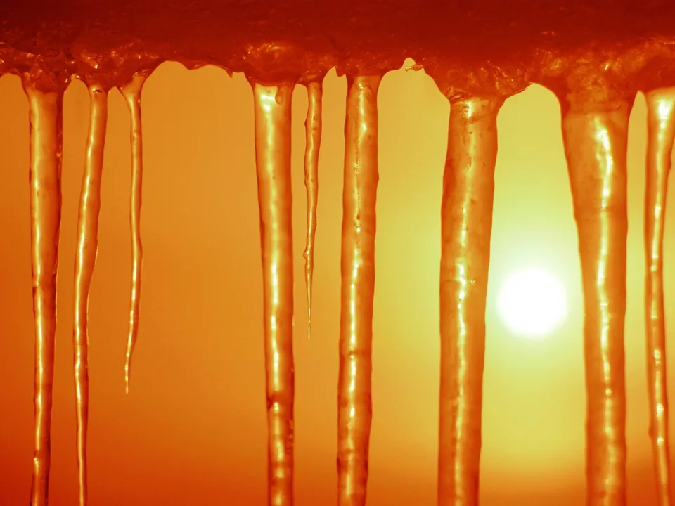 Close-up of icicles hanging and melting, with a bright sun visible in the background.