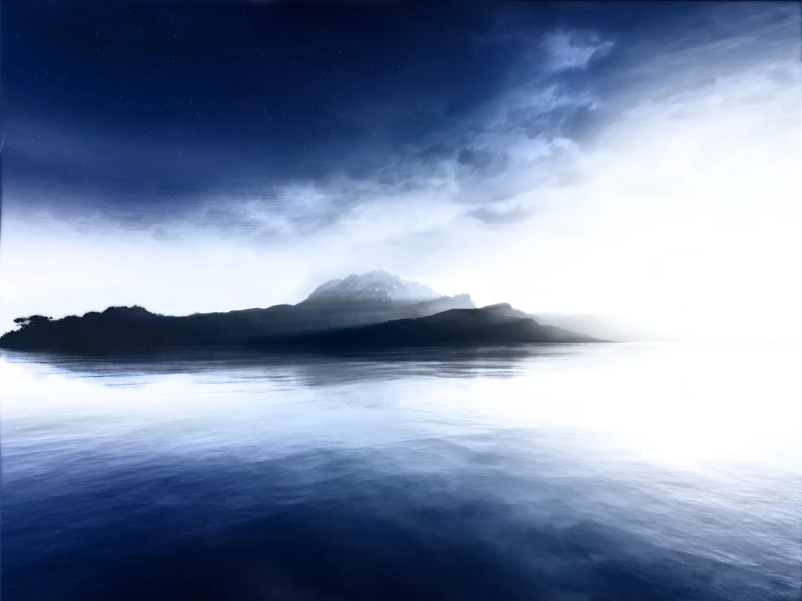 A dark silhouette of a misty mountain island is reflected in the calm, dark blue water under a starry, cloudy sky.