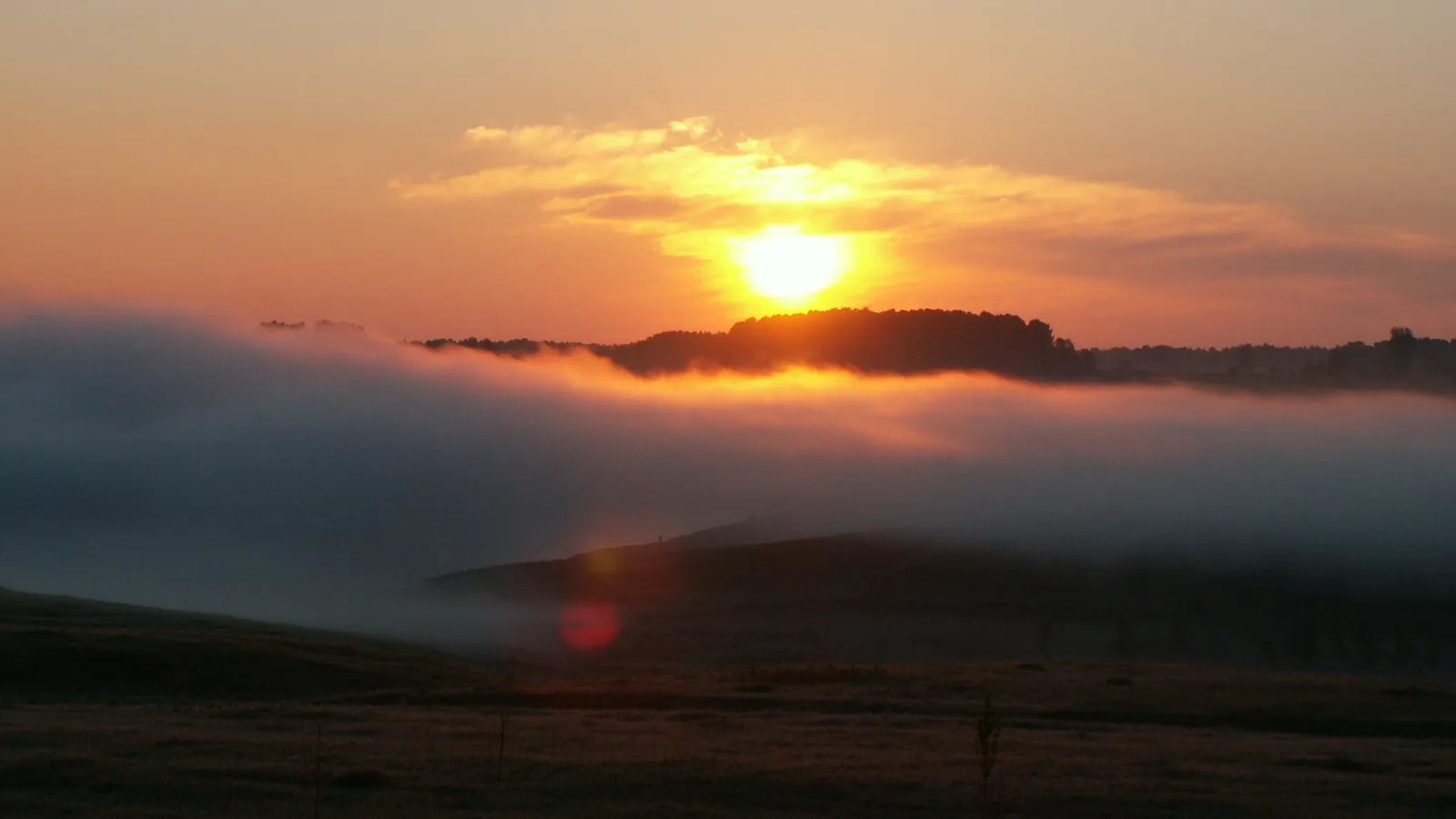 The sun rises over a misty landscape of rolling hills and trees.