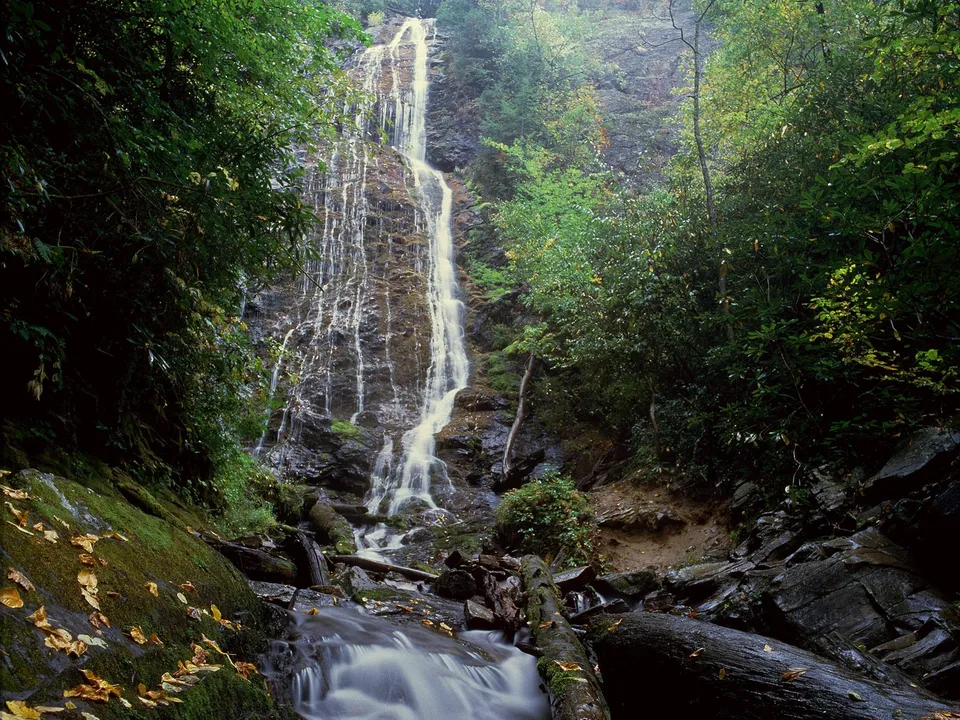 A tall, slender waterfall flows down moss-covered rocks, appearing misty due to a long exposure.