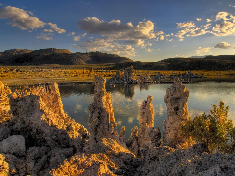 Tufa towers on the shore of Mono Lake illuminated by golden hour sunlight, with mountains in the background.