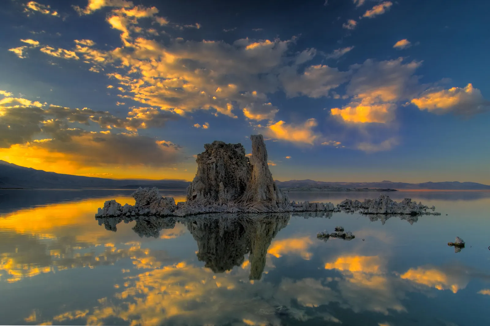 Tufa towers rise from the calm waters of Mono Lake reflecting the golden sunrise and clouds.
