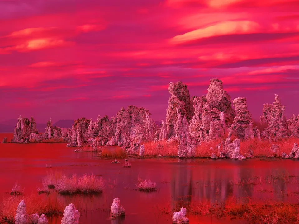 Tufa towers rise from a lake under a vibrant red sky with dramatic clouds.