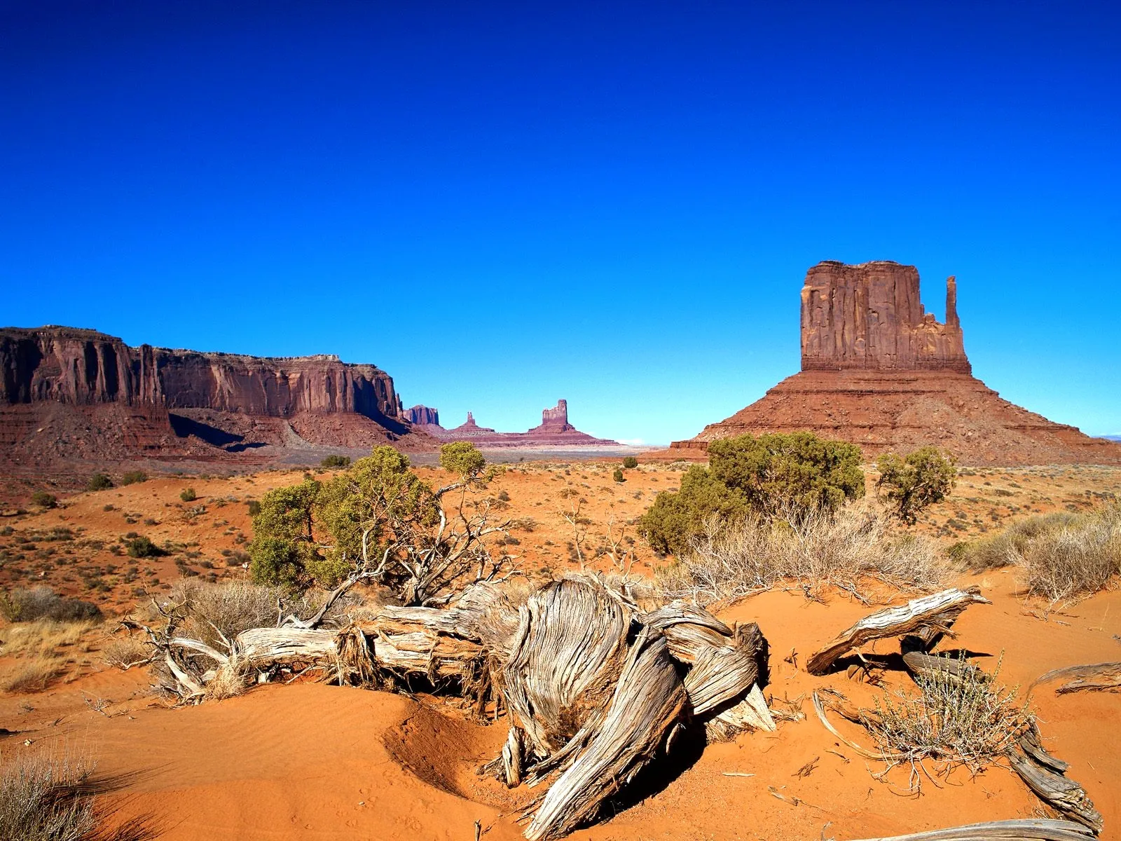 Iconic sandstone buttes rise from a desert landscape under a clear blue sky.