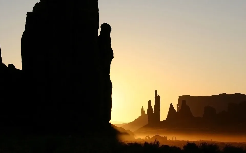 Silhouetted Monument Valley buttes against a hazy sunrise sky with mist.