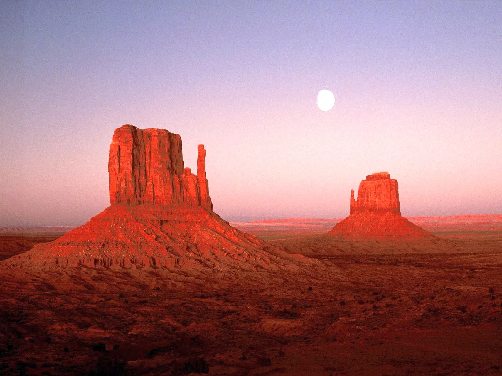 Two large sandstone buttes stand in Monument Valley, illuminated by the soft light of sunset.