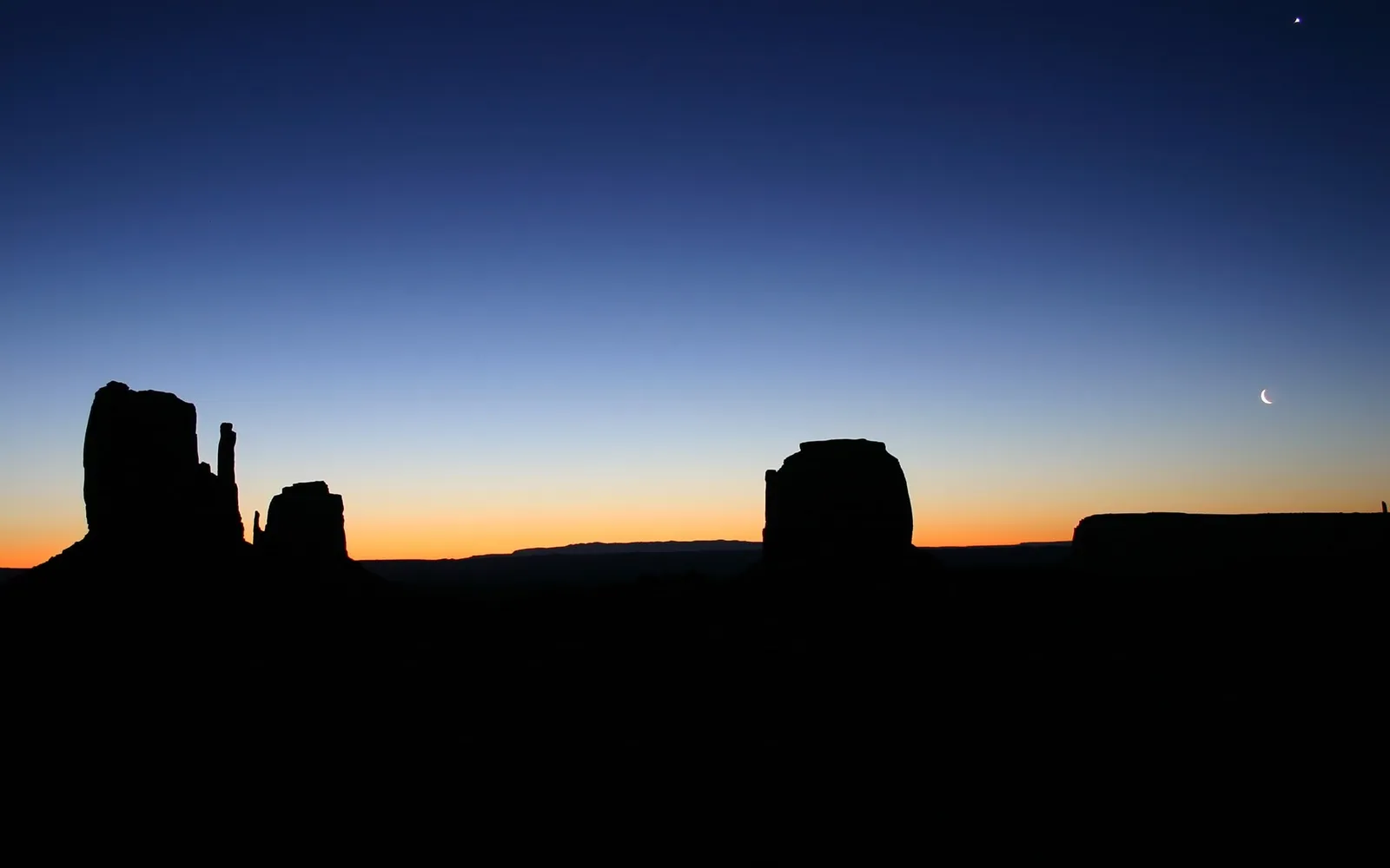 Silhouettes of iconic buttes in Monument Valley against a gradient sky with a crescent moon and a small star.