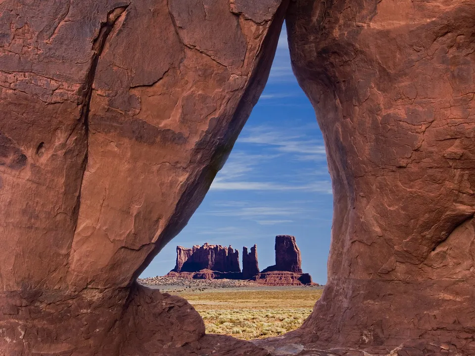 View of Monument Valley's iconic buttes through a large natural sandstone arch.