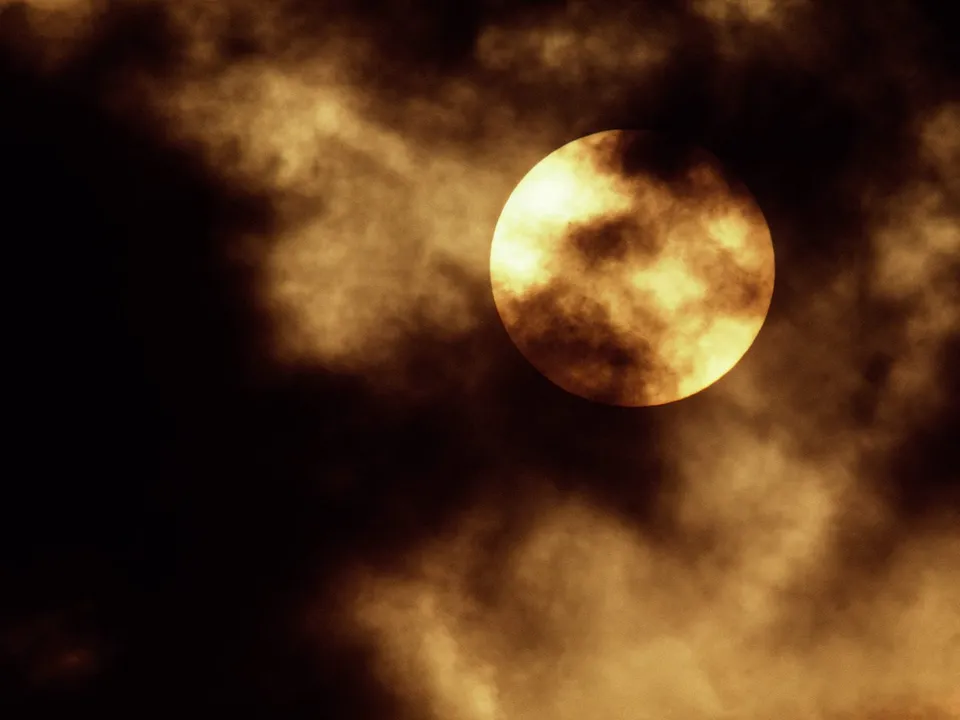 A full moon is partially obscured by dark, textured clouds, creating a dramatic and mysterious atmosphere.