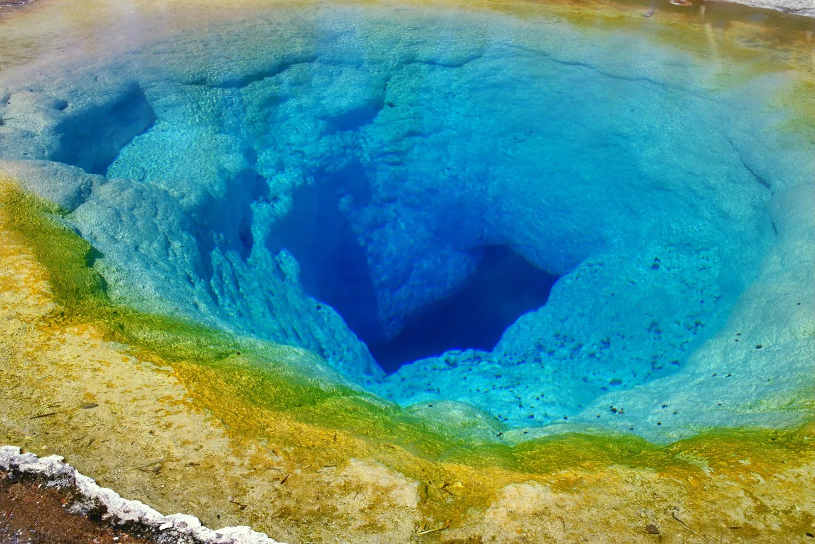 A vibrant hot spring with deep blue water surrounded by yellow and green mineral deposits.