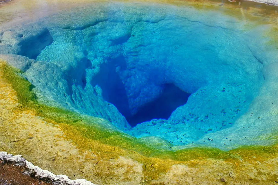 A vibrant hot spring with deep blue water surrounded by yellow and green mineral deposits.