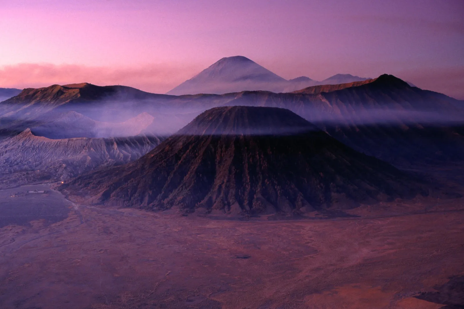 A misty dawn view of Mount Bromo and surrounding volcanoes with a purple sky.