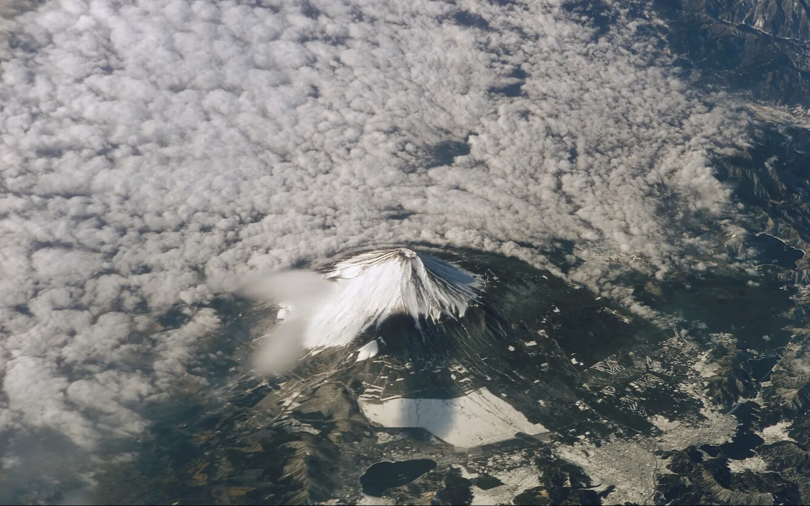 An aerial view of Mount Fuji, a snow-capped volcano, partially obscured by clouds.