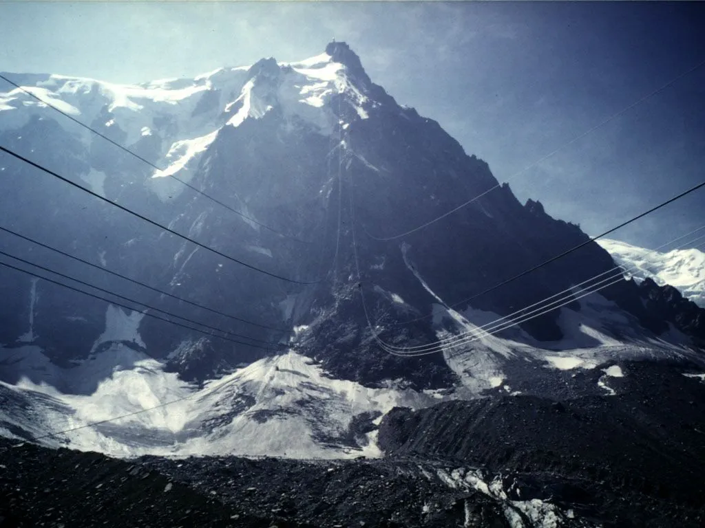 A view of snow-capped mountains with a cable car system visible against a clear blue sky.