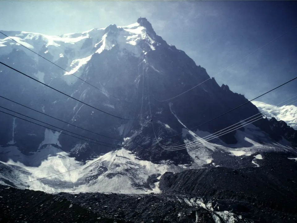 A view of snow-capped mountains with a cable car system visible against a clear blue sky.