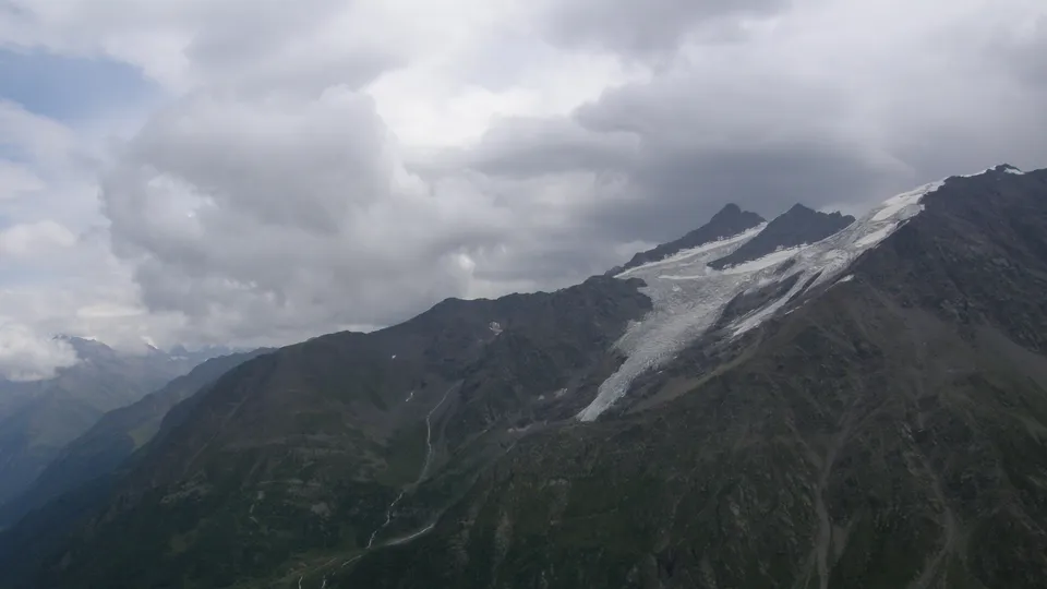 A vast mountain range with a prominent glacier flowing down its side under a cloudy sky.