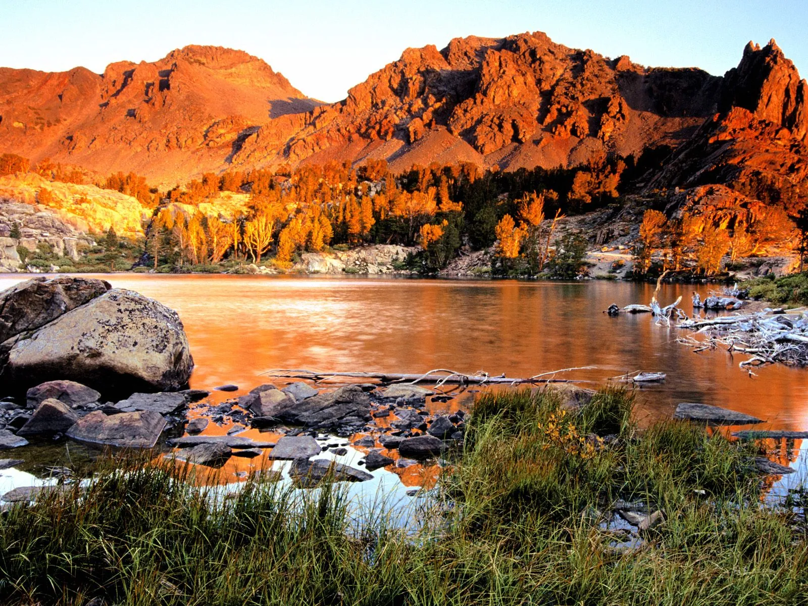 A serene mountain lake reflects the warm glow of sunset on rugged peaks and trees.