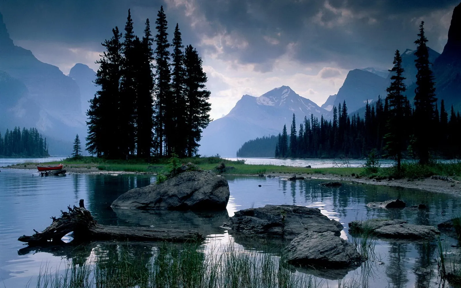 A serene mountain lake with dark pine trees on the shore and a red canoe docked.