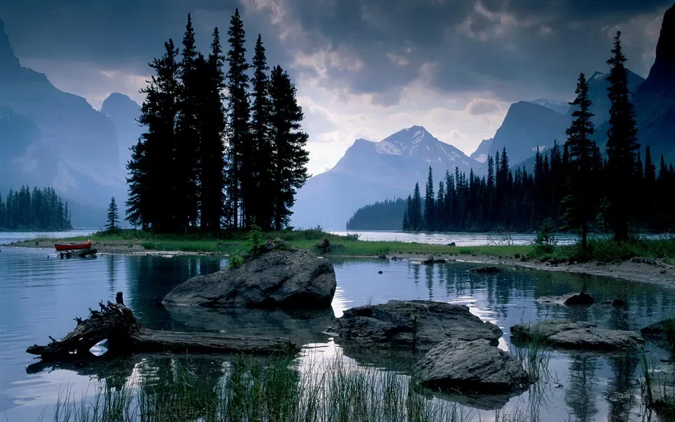 A serene mountain lake with dark pine trees on the shore and a red canoe docked.