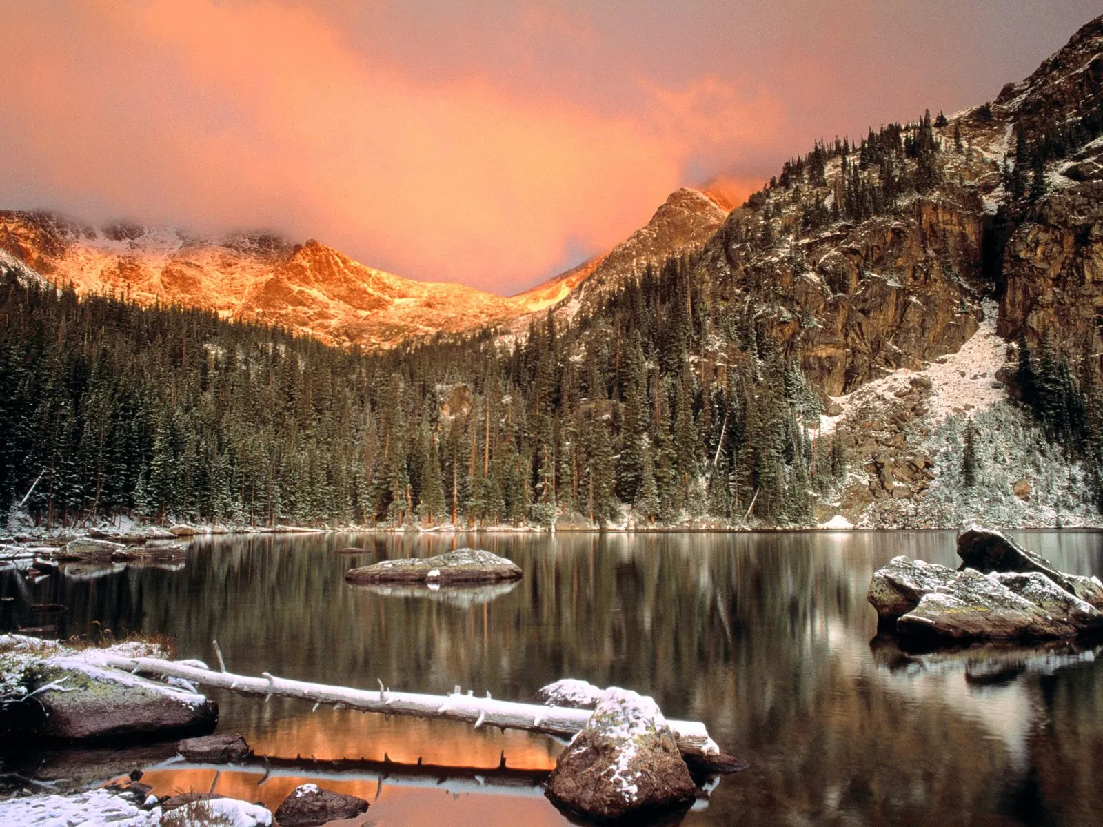 A serene mountain lake reflects snow-dusted peaks and a vibrant sunrise sky.