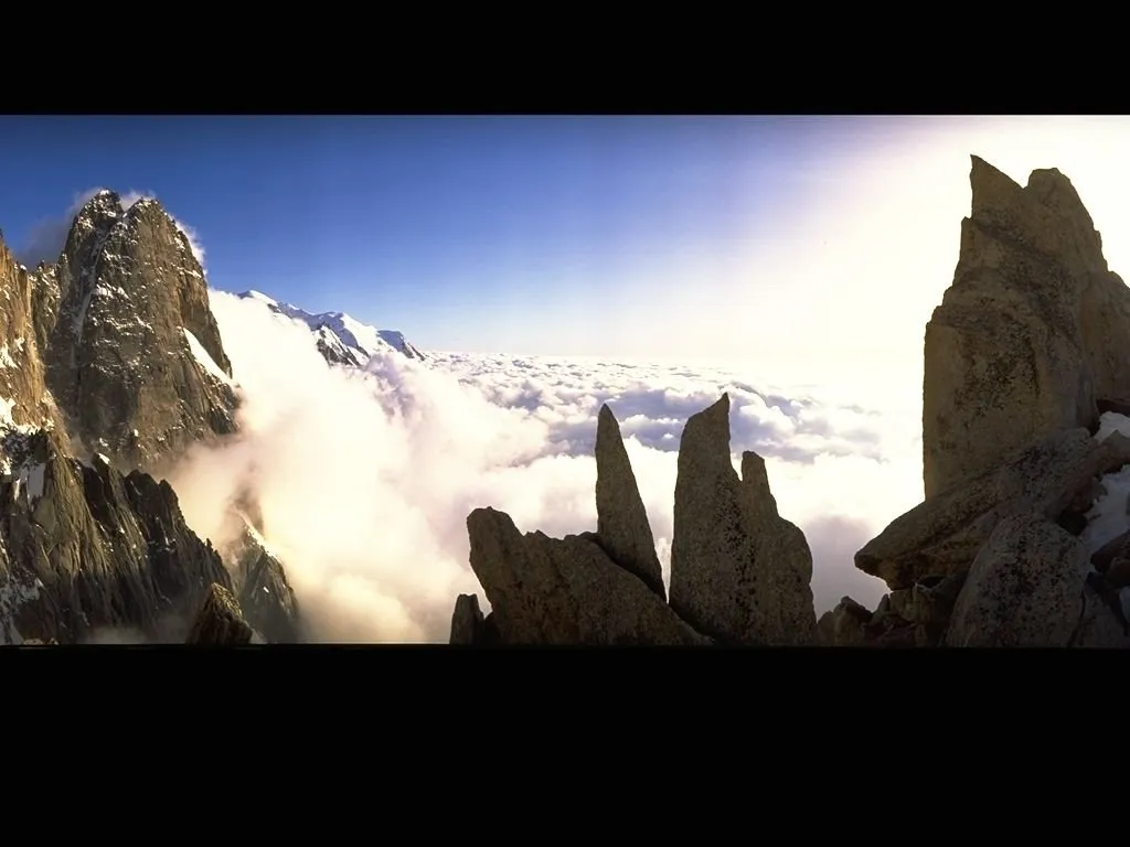 Jagged mountain peaks rise above a vast expanse of white clouds under a clear blue sky.