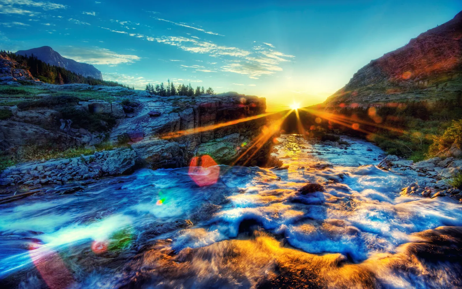 A vibrant sunrise illuminates a fast-flowing river in a mountainous landscape.