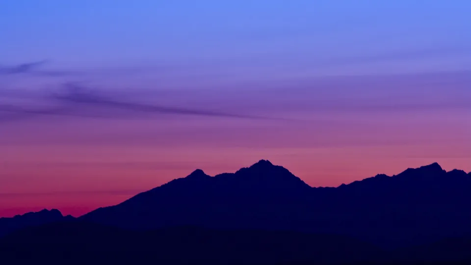 A dark silhouette of jagged mountain peaks against a gradient sky of deep purple and pink.