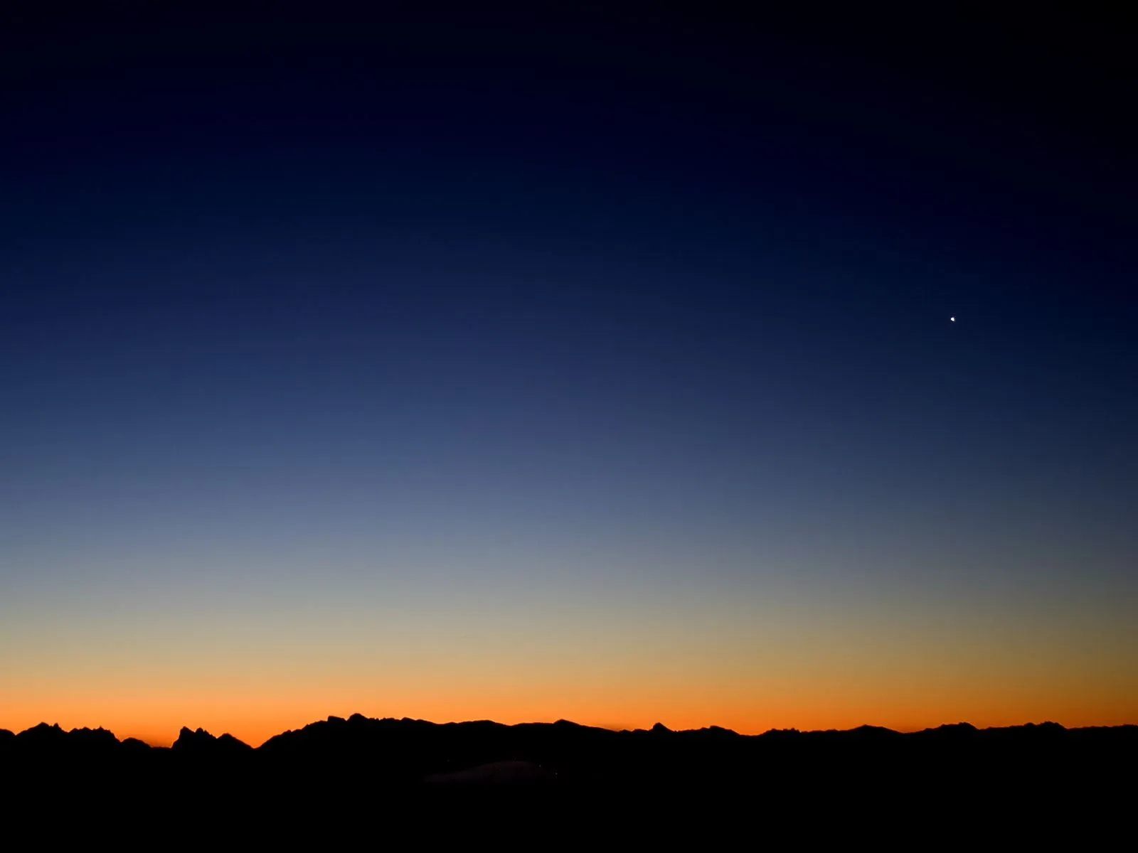 A dark silhouette of a mountain range against a gradient sky of deep blue and orange, with a single bright star visible.