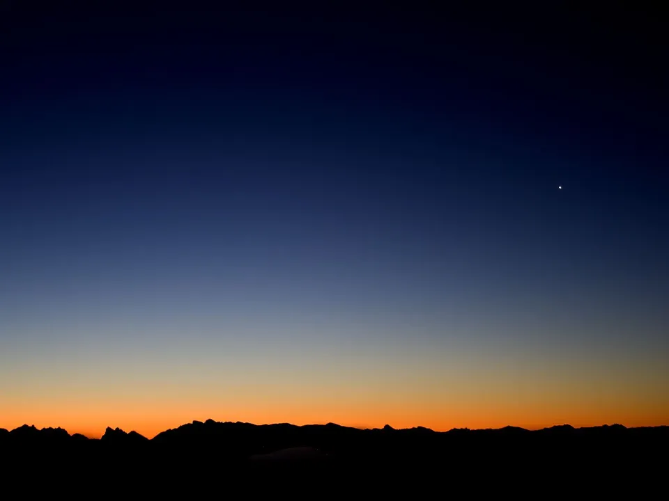 A dark silhouette of a mountain range against a gradient sky of deep blue and orange, with a single bright star visible.