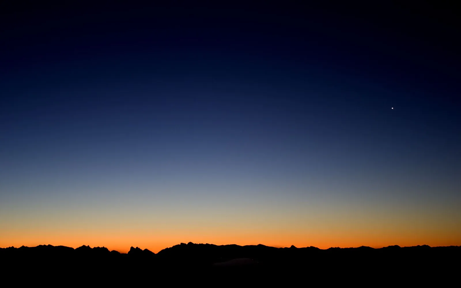 A dark silhouette of a mountain range against a gradient sky transitioning from deep blue to orange.