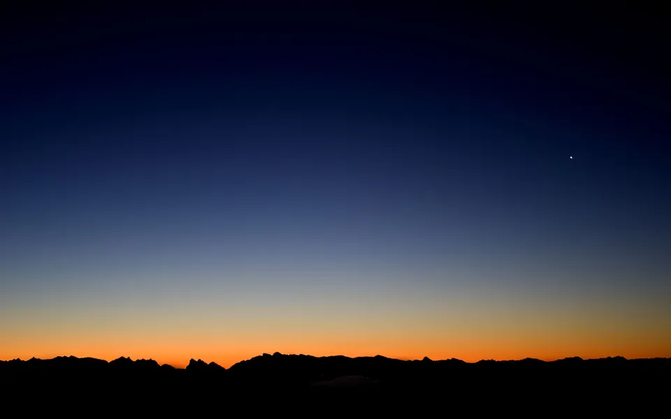 A dark silhouette of a mountain range against a gradient sky transitioning from deep blue to orange.