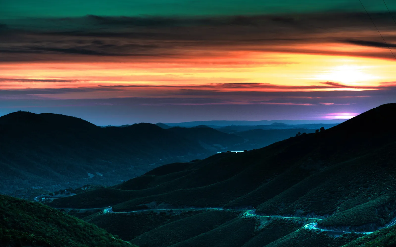 A vibrant sunset paints the sky with orange, pink, and yellow hues over silhouetted mountain ranges.