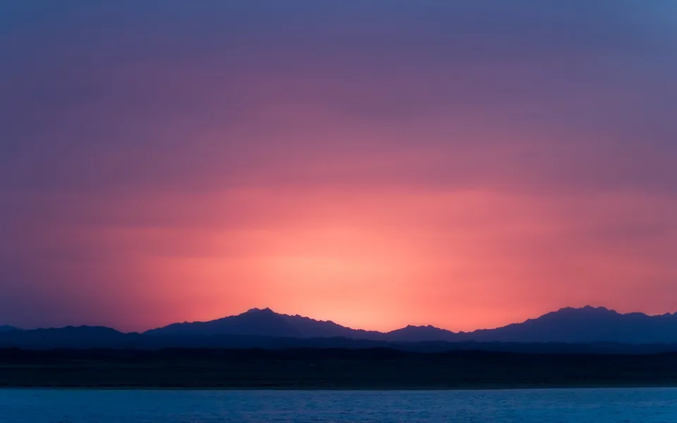 A vibrant sunset paints the sky in shades of pink and purple over a silhouetted mountain range and a body of water.