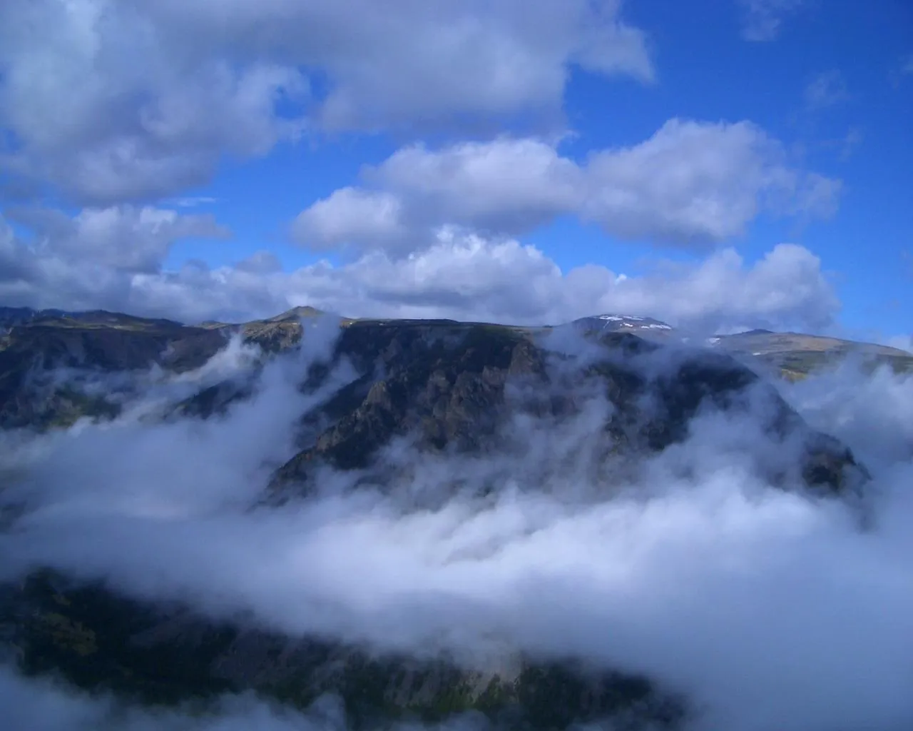 Thick white clouds drift through a rugged mountain valley, obscuring the lower slopes and revealing peaks above.