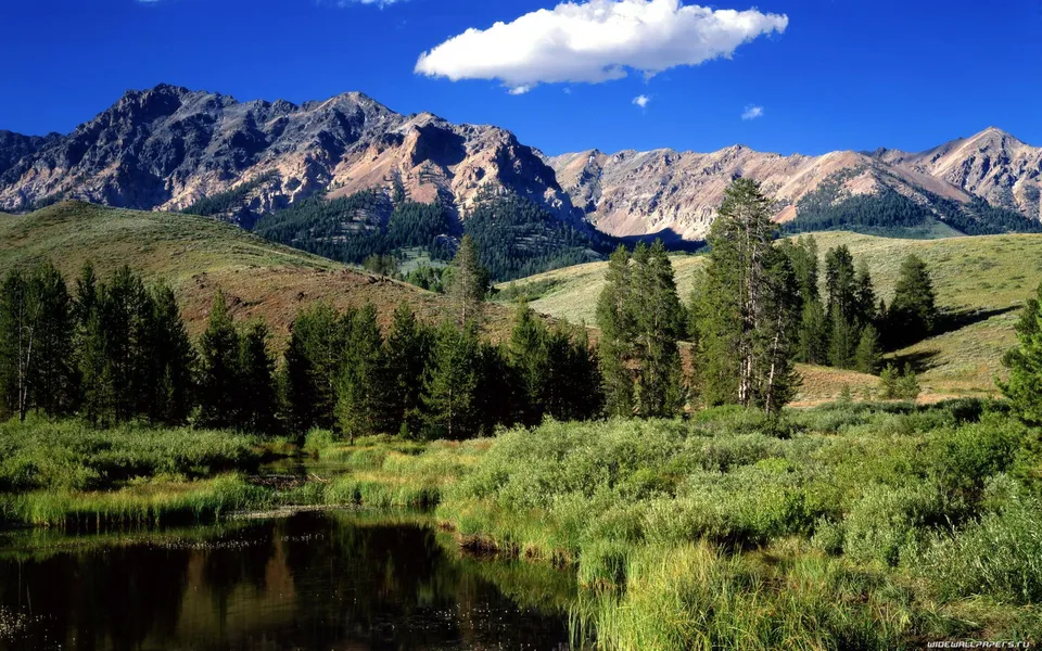 A wide mountain range with rocky peaks under a bright blue sky with a single white cloud.