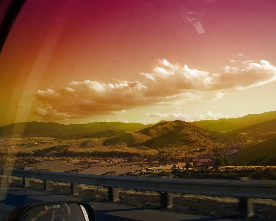 View of rolling hills and mountains from a car window during a colorful sunset.