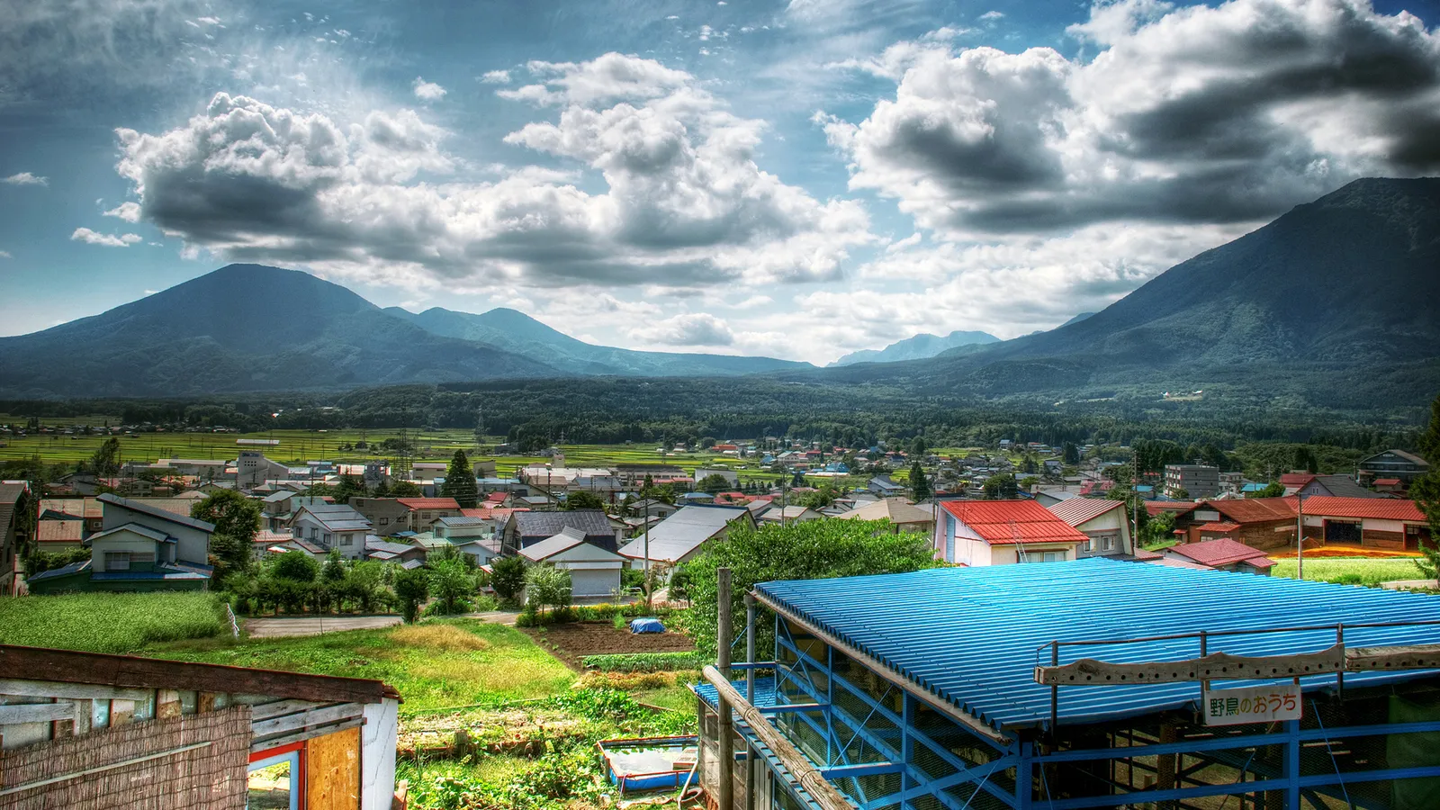 A wide shot of a village with mountains in the background and a cloudy sky.