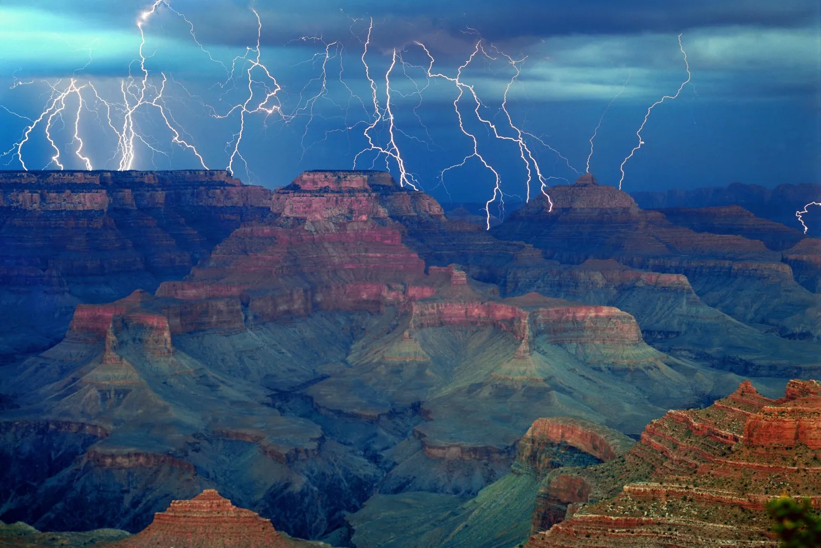 Multiple lightning strikes illuminate a stormy sky over the Grand Canyon.