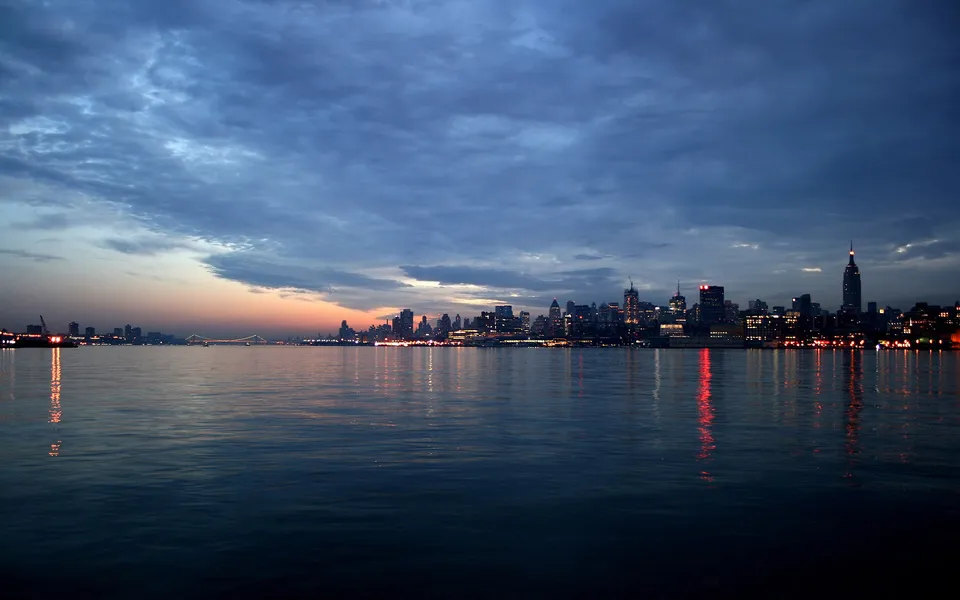 New York City skyline at dusk with colorful sky and water reflections.