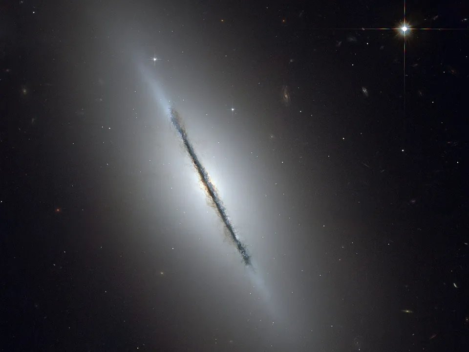A lenticular galaxy, NGC 5866, is viewed edge-on, revealing a prominent dust lane bisecting its bright core.