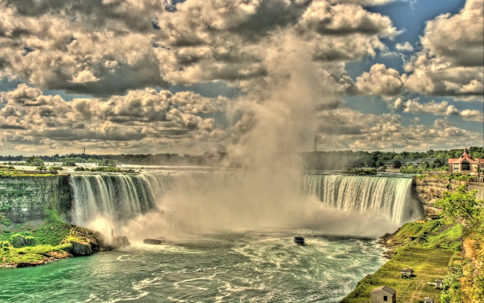 A wide view of Niagara Falls with mist rising and a cloudy sky overhead.