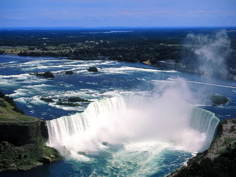 An aerial view of Niagara Falls with mist rising from the powerful cascade and turbulent water below.
