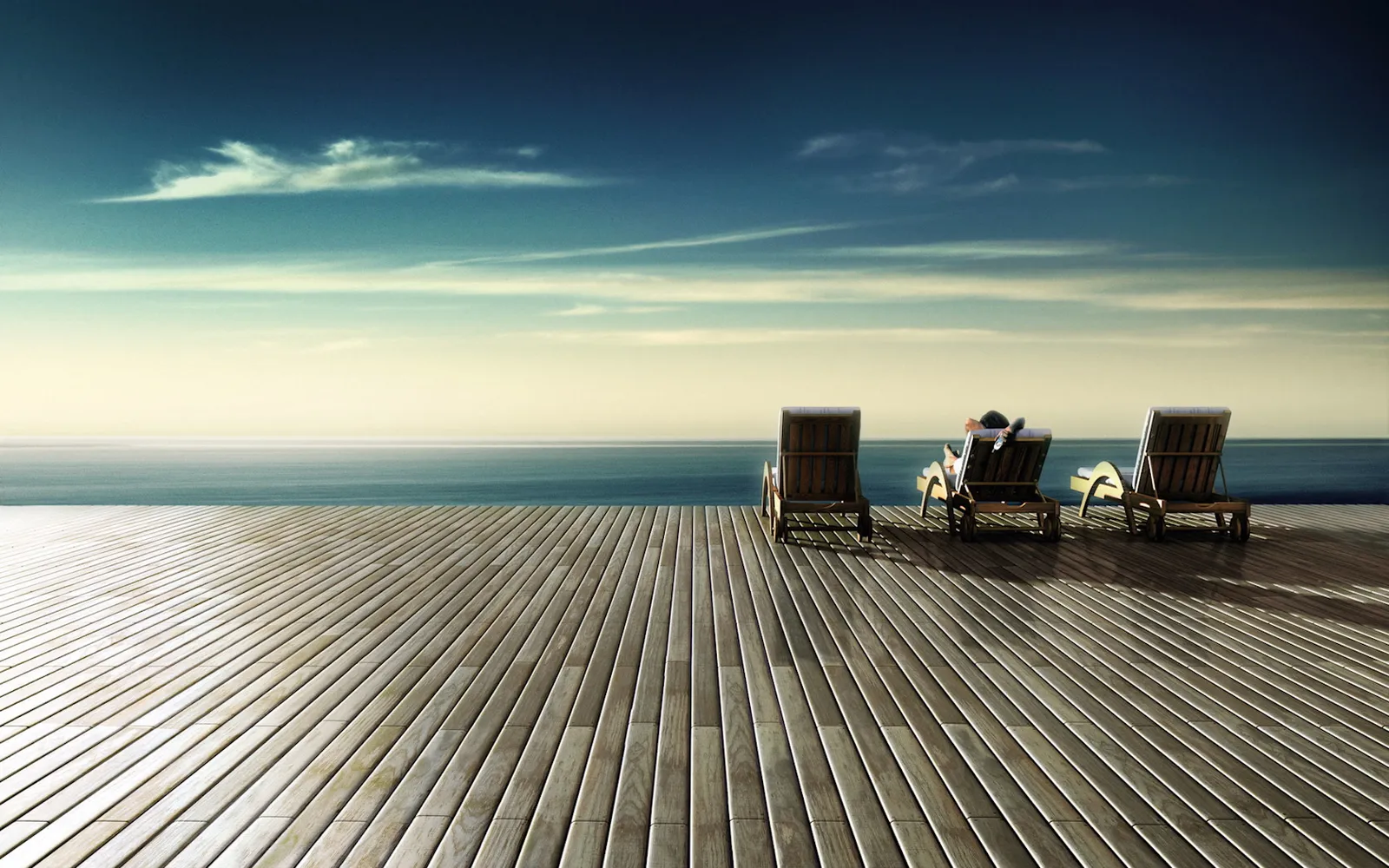 Three lounge chairs on a wooden deck overlooking the ocean, with one person relaxing in a chair.