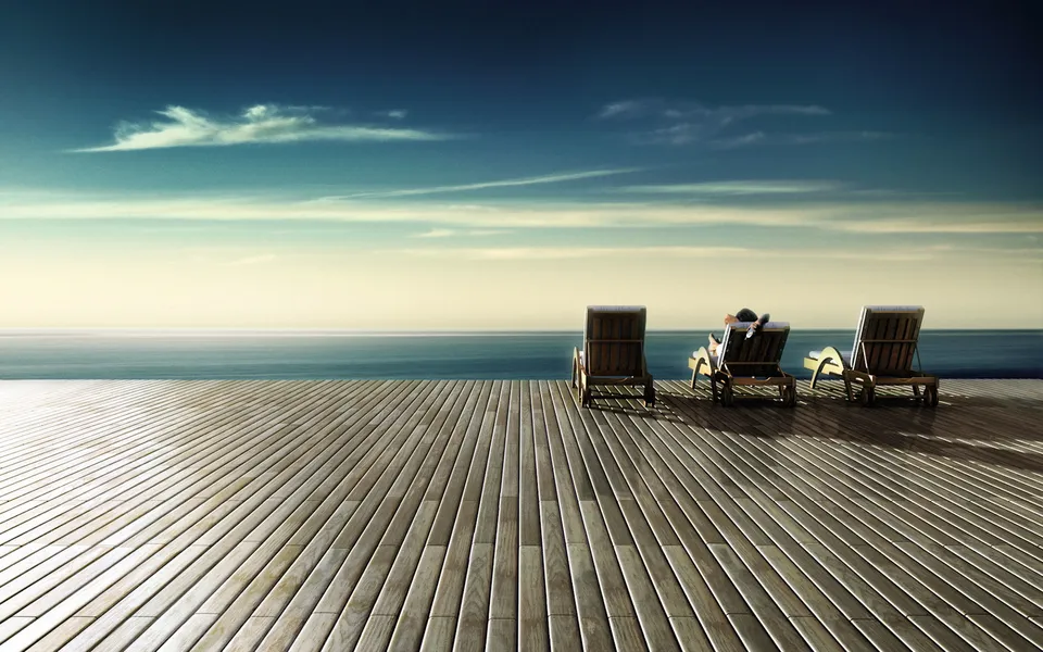 Three lounge chairs on a wooden deck overlooking the ocean, with one person relaxing in a chair.