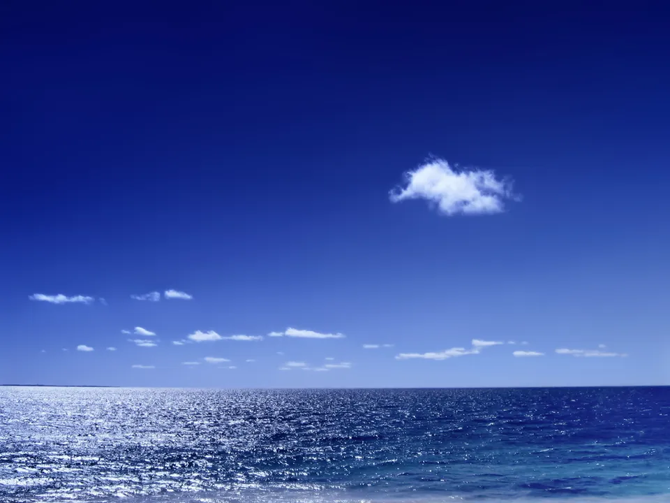 A wide expanse of deep blue sky with scattered white clouds above a shimmering blue ocean.