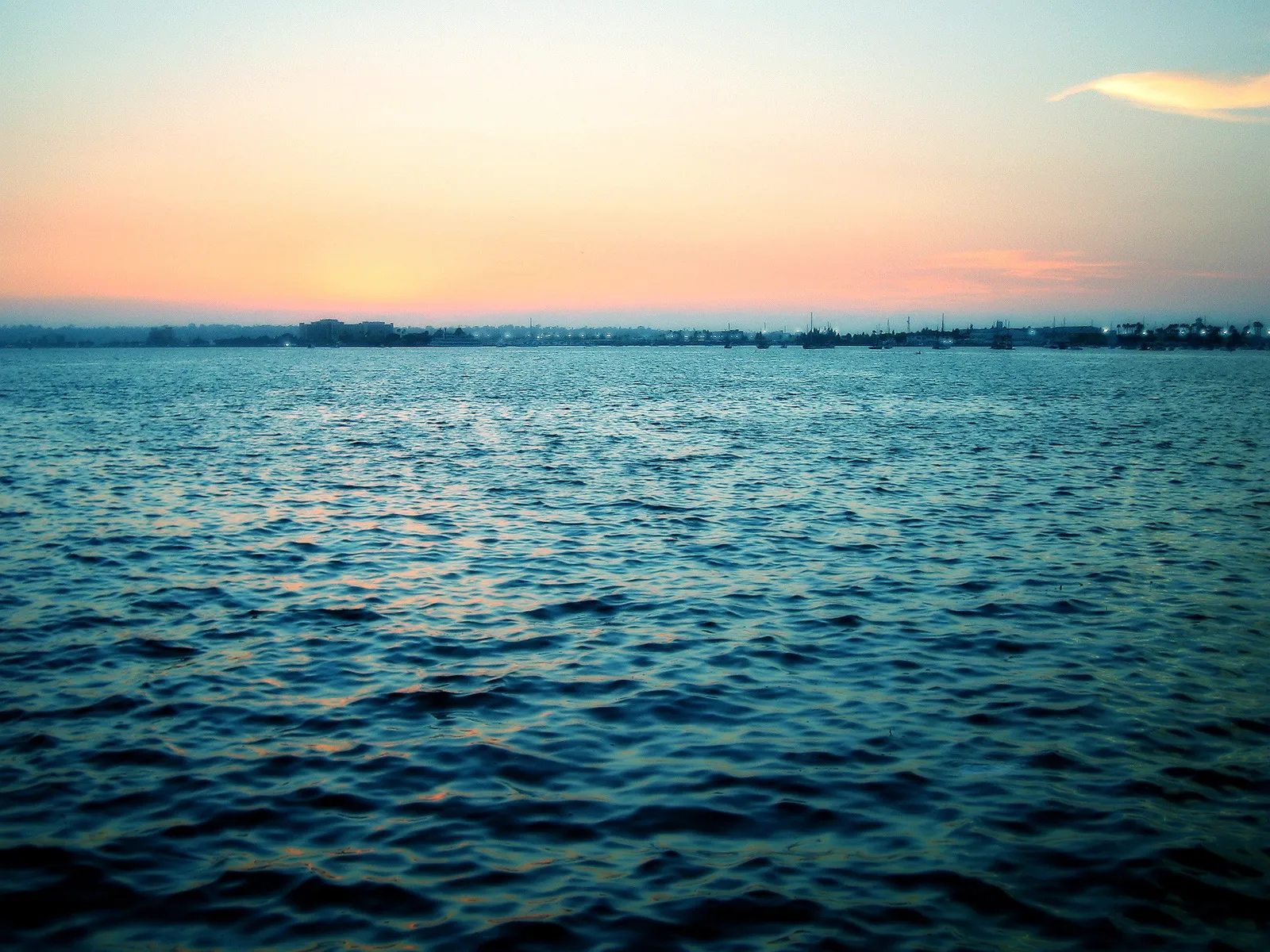 A wide expanse of blue water stretches towards a hazy horizon with a soft orange and pink sunset sky.