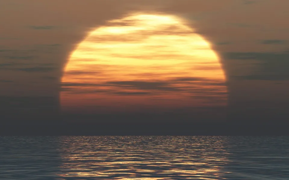 A large, bright sun is setting over a calm ocean, casting golden and orange light through the clouds.