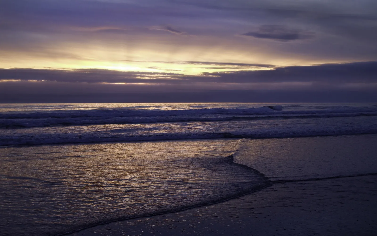 A serene ocean sunset with purple clouds and golden light breaking through.