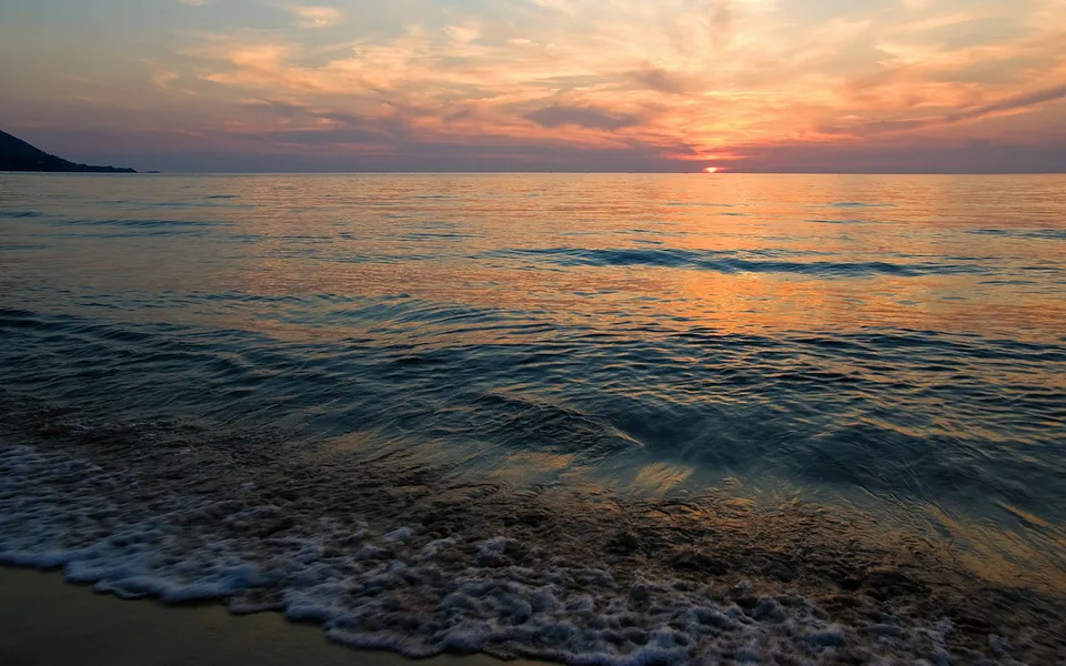The sun sets over the ocean, casting golden light on the water and clouds.
