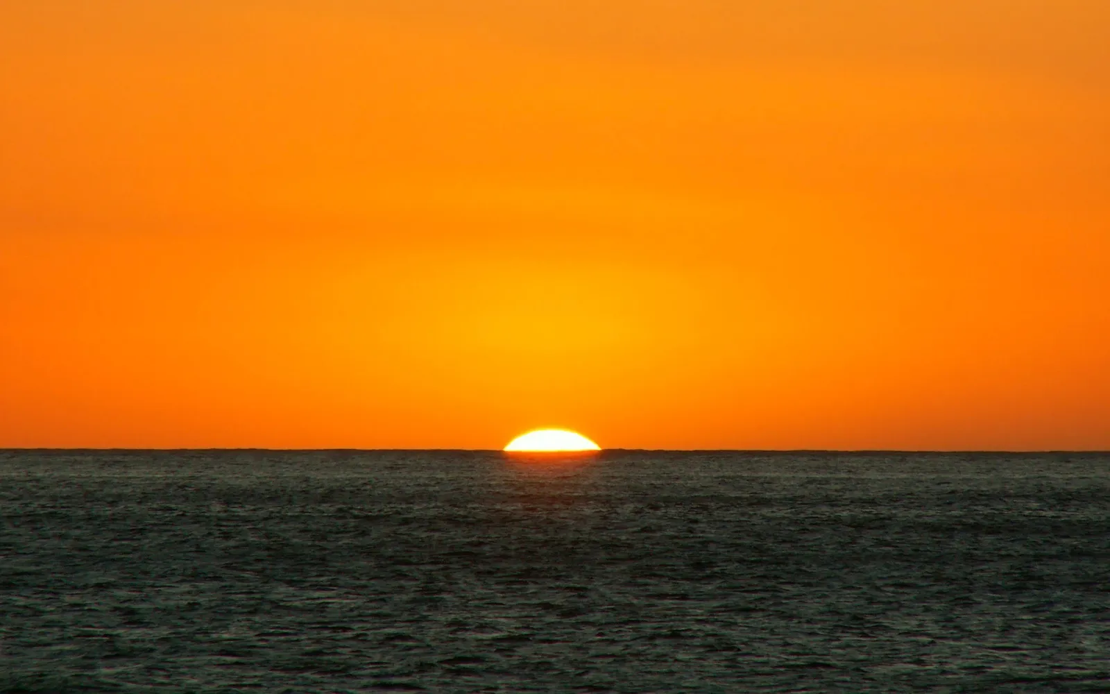 The sun is setting over the ocean, casting a vibrant orange glow across the sky.